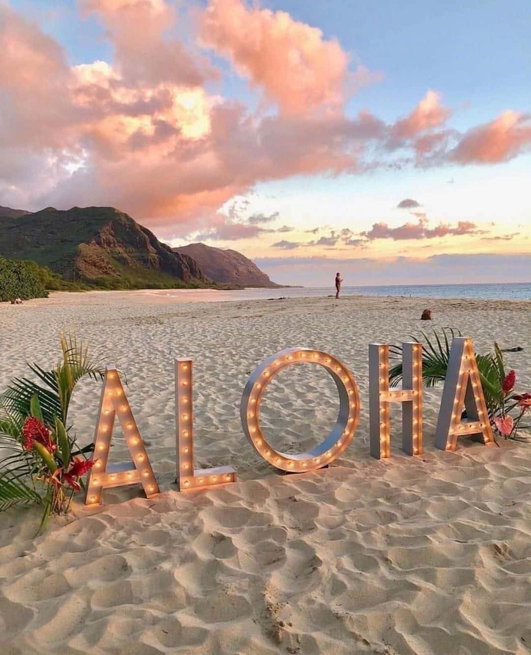 Lighted ALOHA sign on a west Oahu beach with mountains at sunset